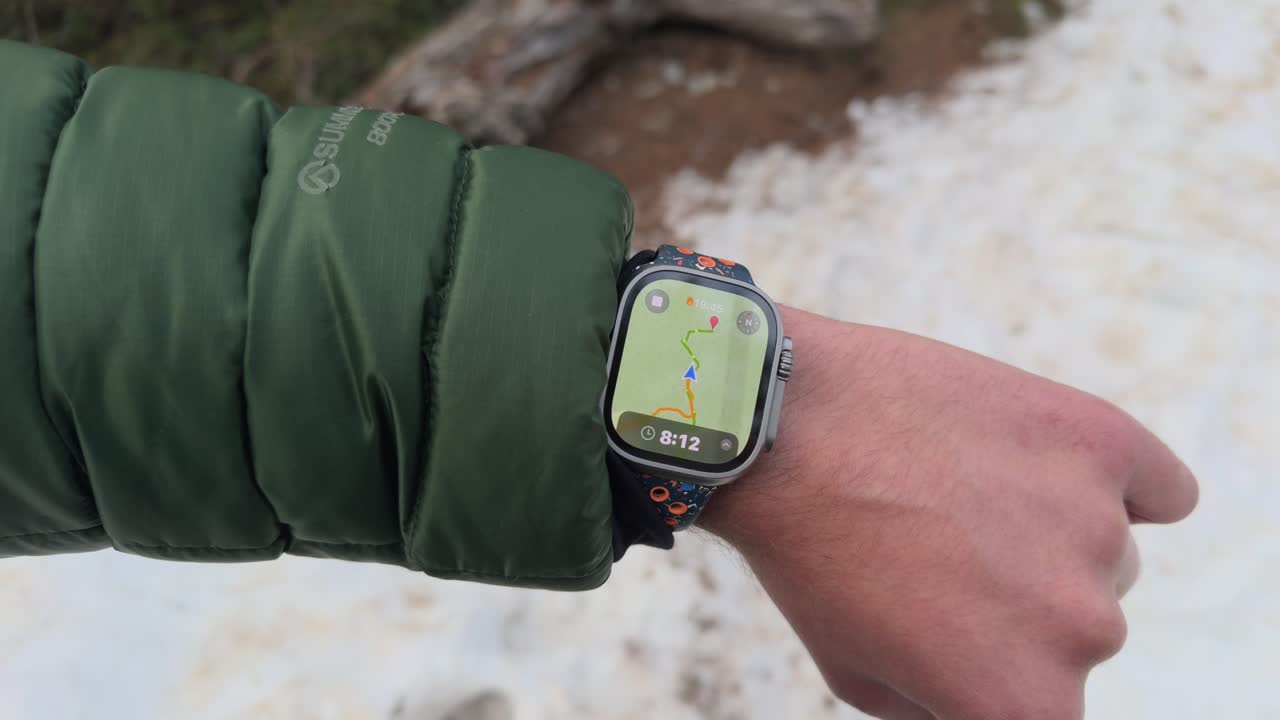 Primo piano di un escursionista che controlla la navigazione GPS su uno smartwatch robusto. Il polso si solleva mentre la mappa guida il percorso durante una passeggiata all'aperto su un sentiero innevato