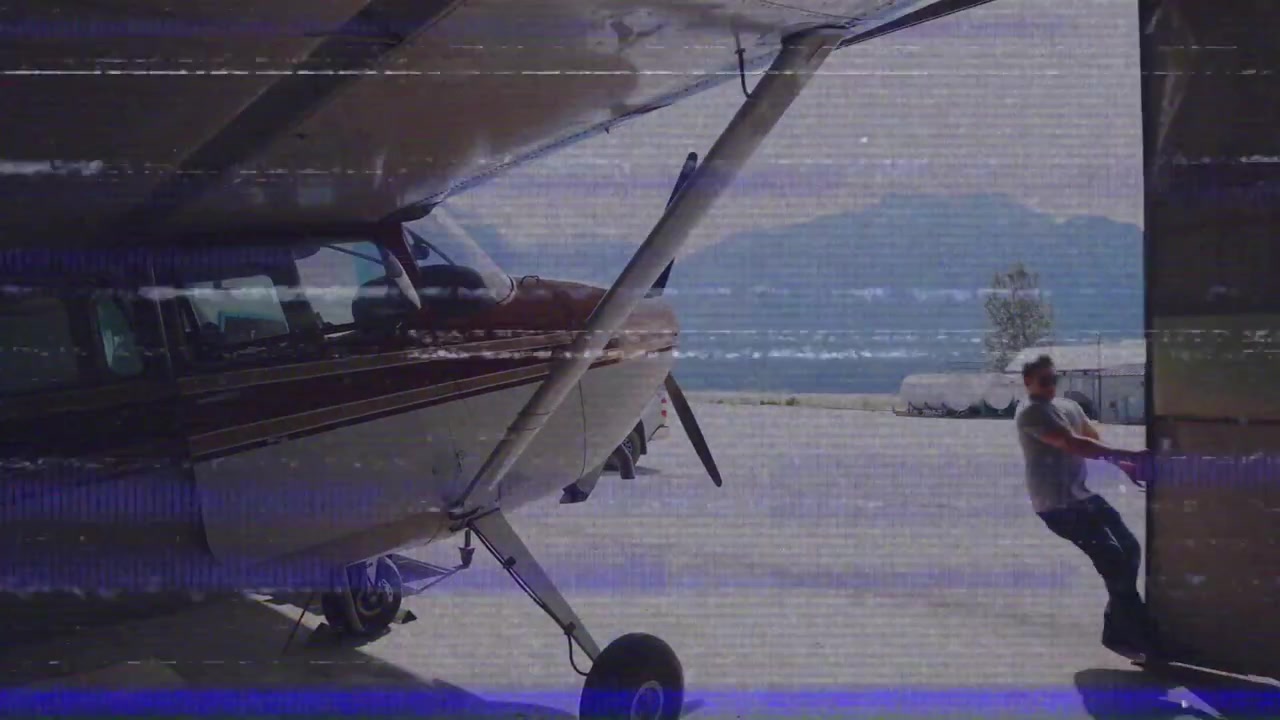 Uomo che apre la porta dell'hangar, rivelando un aereo a elica in un hangar aeronautico con dati di volo animati.