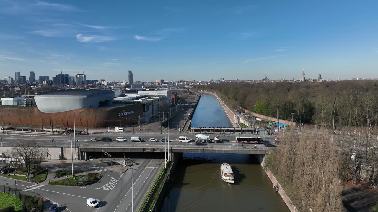 Ascending aerial movement above canal with a boat sailing under bridge in Brussels, Belgium, with cityscape views
