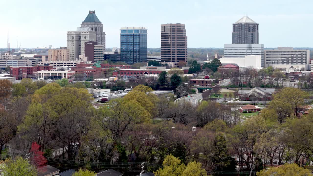 Veduta aerea che si spinge nello skyline di Greensboro, NC, sopra le cime degli alberi in primavera.