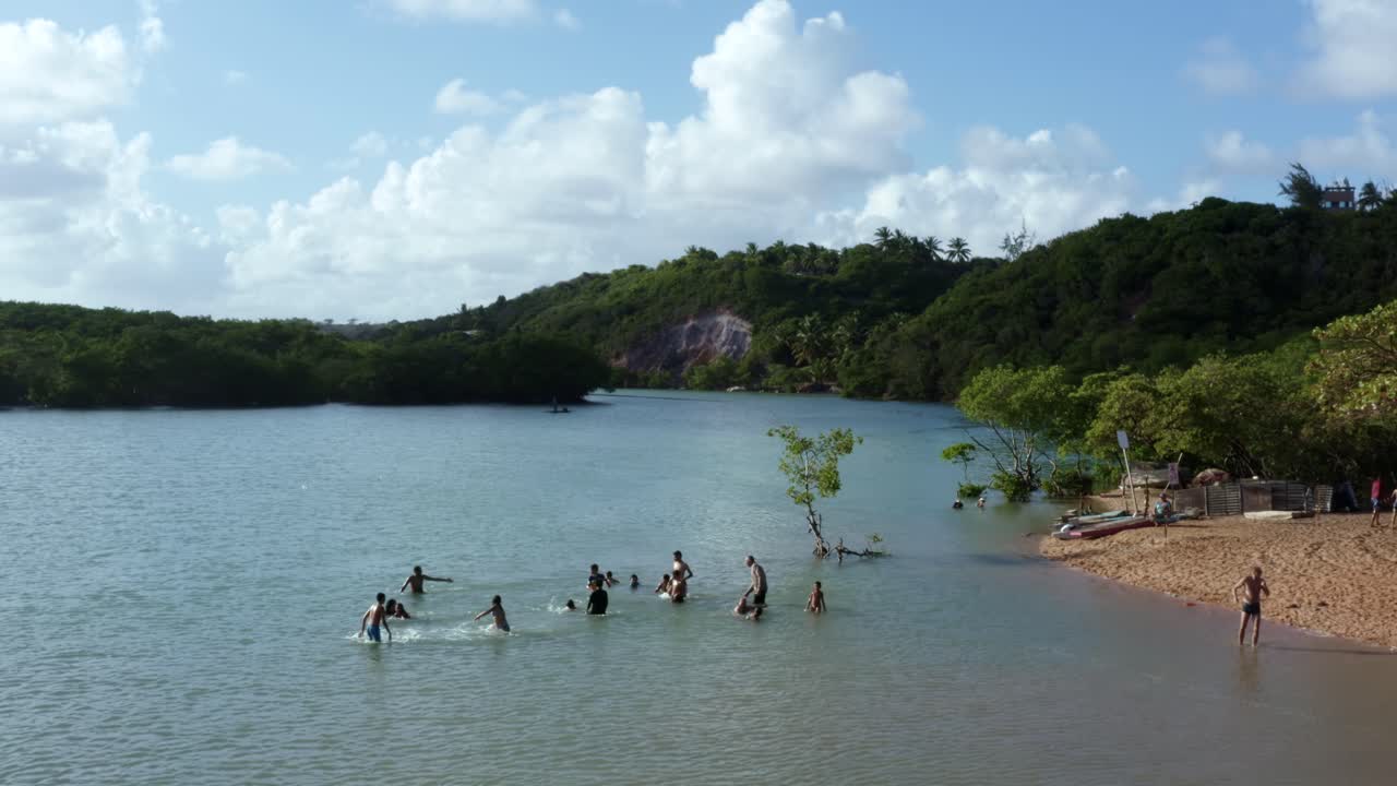브라질 파라이바에 있는 열대 해변 수도인 조앙 페소아 근처 구불구불한 열대 그라마메 강의 물에서 노는 작은 그룹의 사람들을 지나는 공중 드론 샷의 돌리