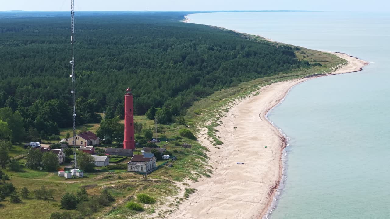 Aerial of Akmenraga lighthouse on Baltic coast with sandy beach and surrounding forest, establishing medium orbit