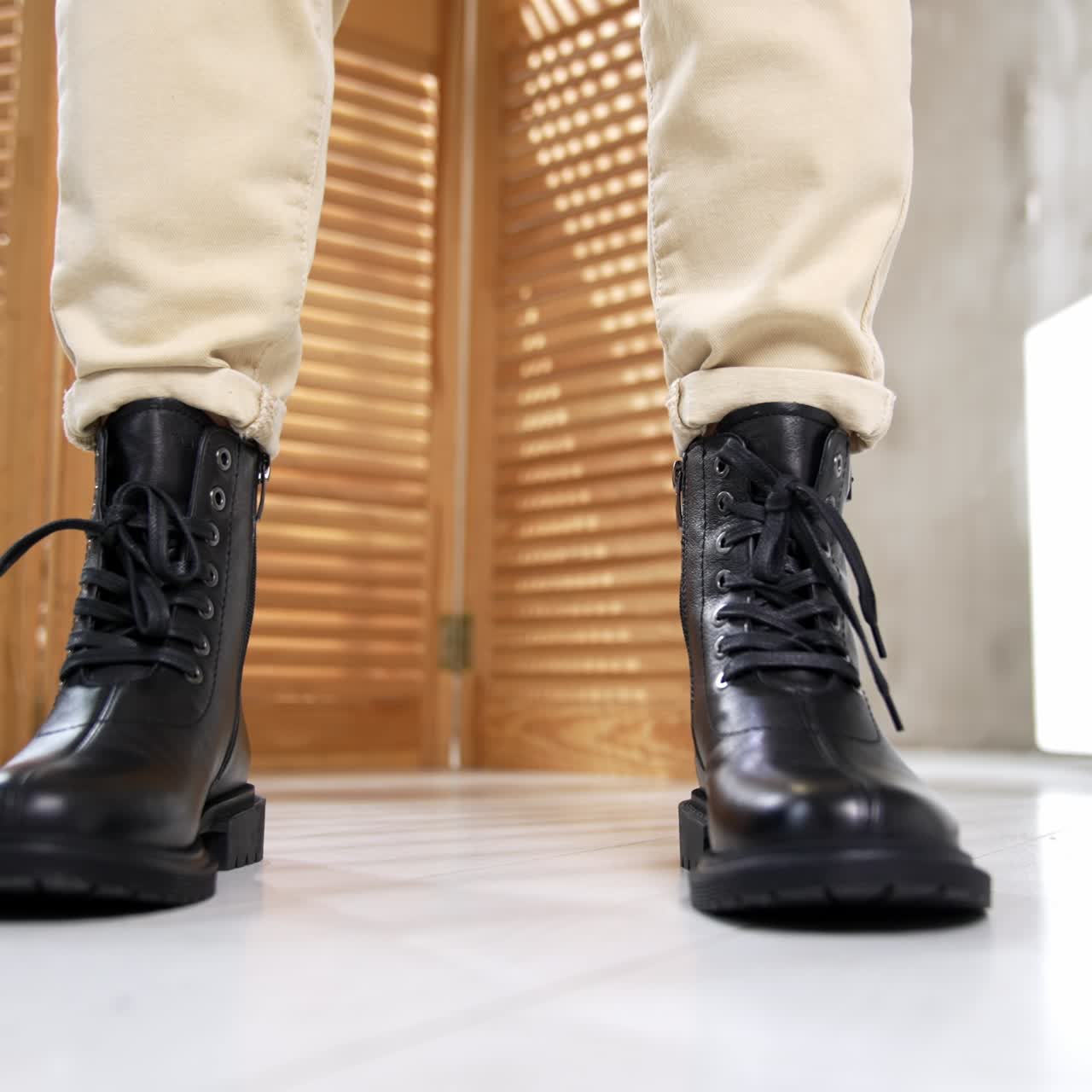 Model wearing light pants demonstrating comfortable warm boots with laces in front of camera. Studio footwear presentation close up