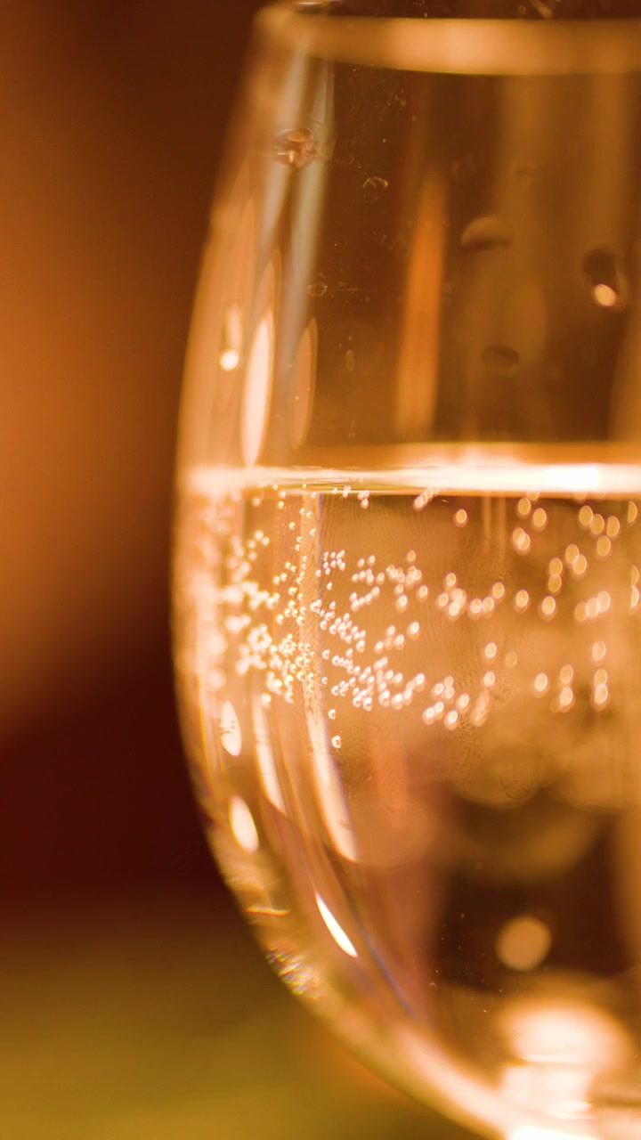 Bolle salgono in un bicchiere d'acqua frizzante, illuminazione bokeh calda, obiettivo macro, atmosfera elegante da bar.