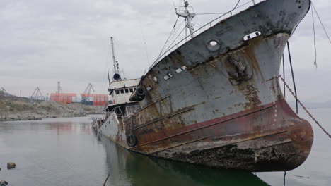 Rusty-grey-half-submerged-shipwreck-anchored-near-the-shore-on-a-cloudy-overcast-day