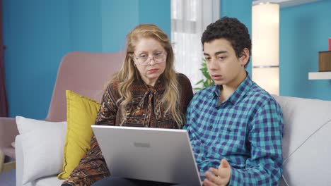 el niño usa una computadora portátil en casa y se lo dice a su madre, que lo está viendo.