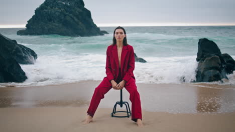 model posing camera coast in red suit. woman sitting chair at ocean vertical