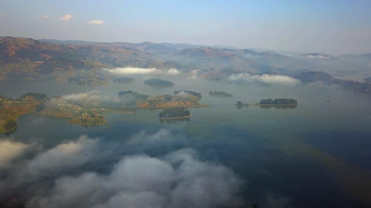 High aerial view over misty Lake Bunyonyi, Uganda, as morning clouds drift between its islands and hills during the cool early dry season, revealing tranquil waters and soft golden light