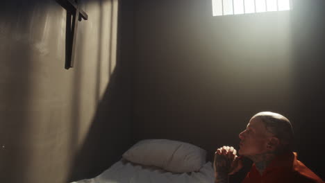 tattooed inmate with shaved head praying deeply in prison cell
