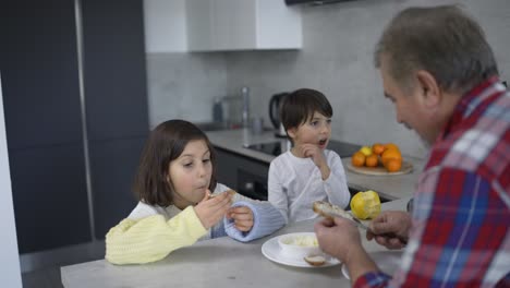 Two-small-children-are-eating-sandwiches-made-by-grandfather