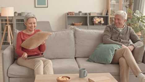 happy senior couple enjoying a pillow fight at home