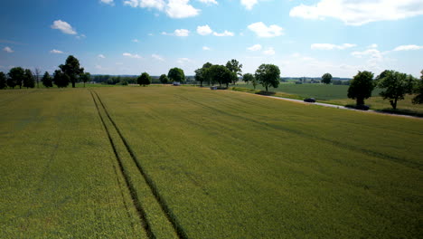 El-Dron-Avanza-A-Lo-Largo-De-Las-Vías-Del-Tractor-Que-Corren-Paralelas-A-La-Carretera-En-Un-Campo-Agrícola-Abierto