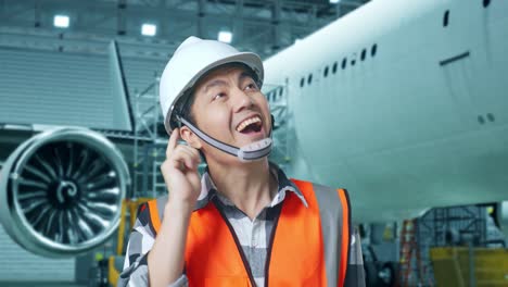 close up de ingeniero masculino asiático con casco de seguridad de pie con aviones en el hangar. pensando en algo y mirando a su alrededor y luego levantando su dedo índice