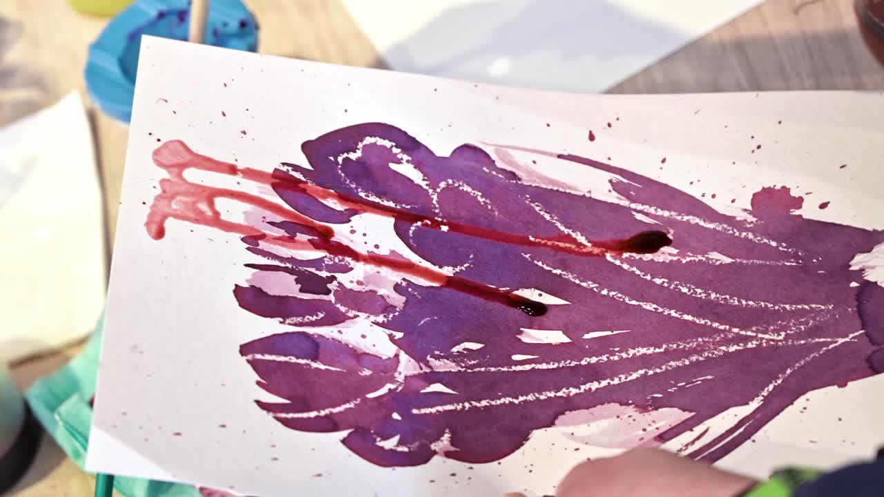 A woman in a studio painting on paper with red wine and brush, close view