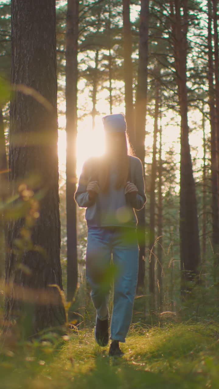 mujer excursionista con mochila camina a través de un bosque pacífico, iluminado por la cálida luz del sol de la noche, rodeada de árboles altos y vegetación suave, se ve reflexiva y conectada con la naturaleza
