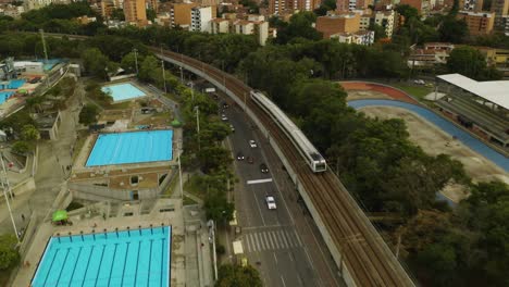 Aerial-Tracking-Shot-of-Subway-Train-Passing-Swimming-Pools-in-Medellin