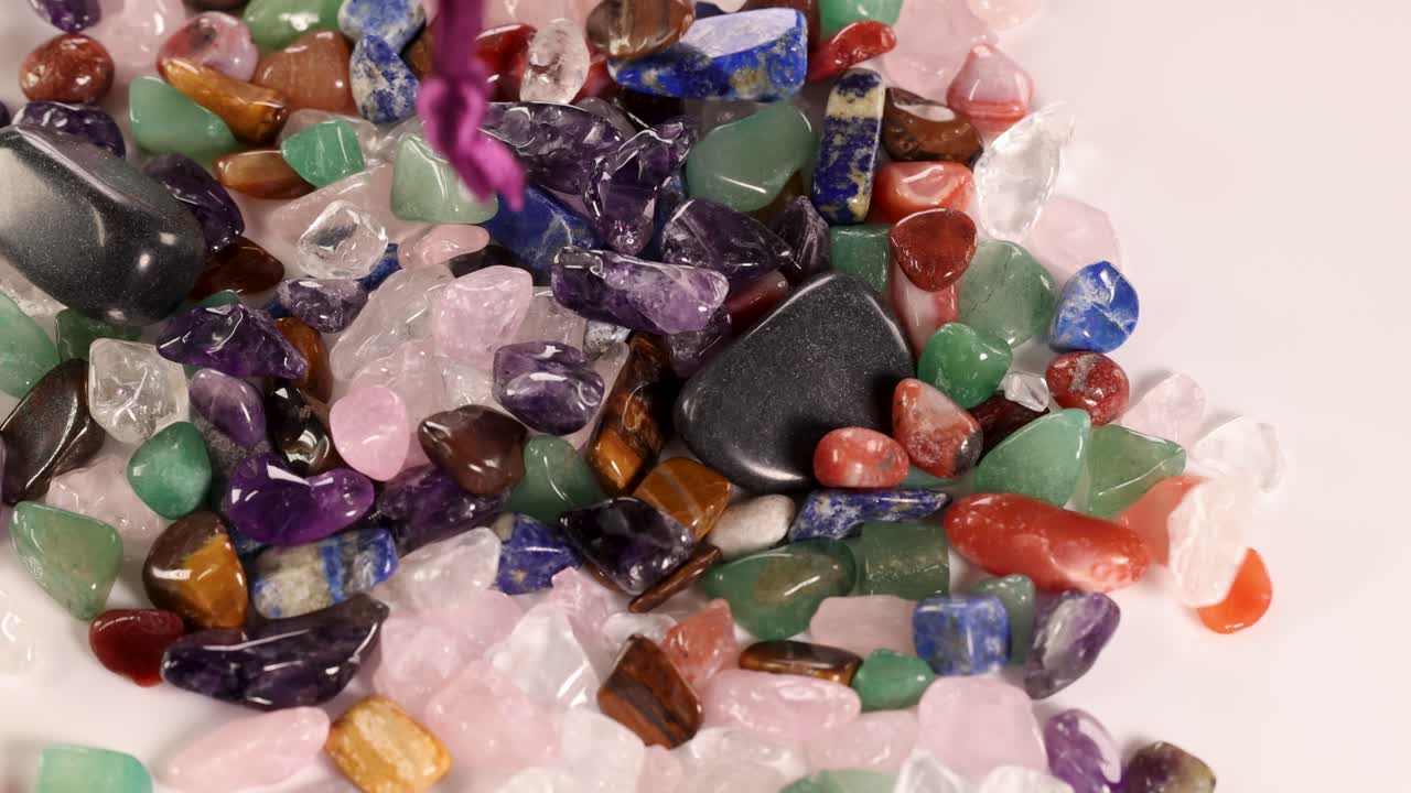 A velvet pouch releases vibrant gemstones onto a surface, showcasing a variety of colors and textures in bright lighting