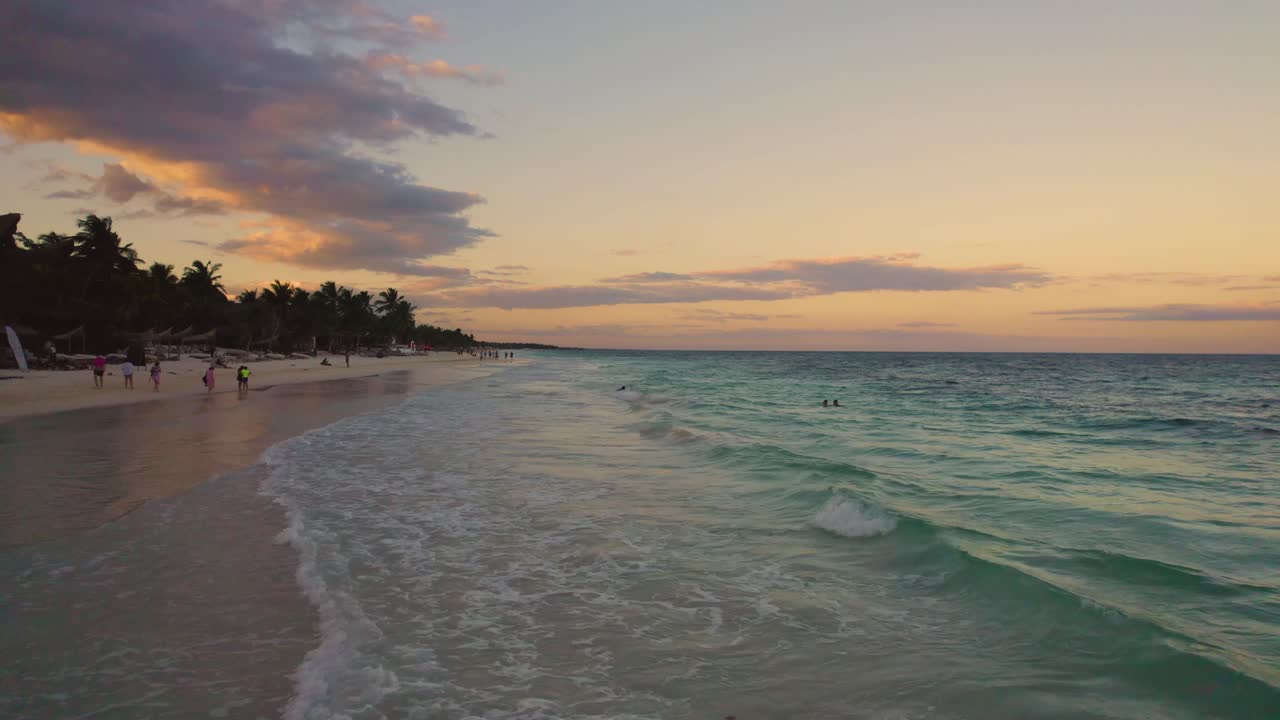 vuelo bajo aéreo sobre las olas del mar caribe en la playa de akiin en tulum, méxico durante la puesta de sol con gente disfrutando de sus vacaciones en la playa
