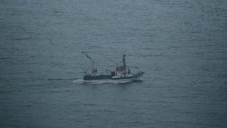 a fishing trawler boat drags it's net in slow motion through calm cold ocean waters on a cold wintery morning