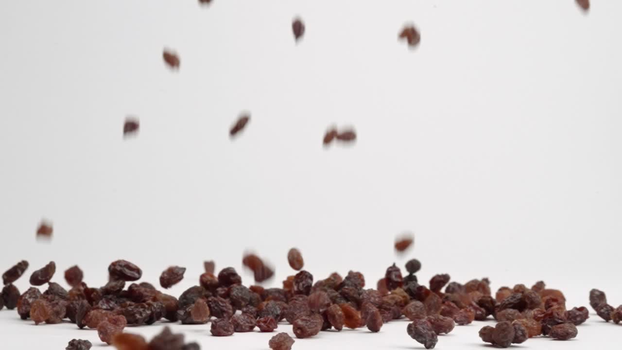 Wrinkly dried red grape raisins falling onto white table top and bouncing into a pile in slow motion