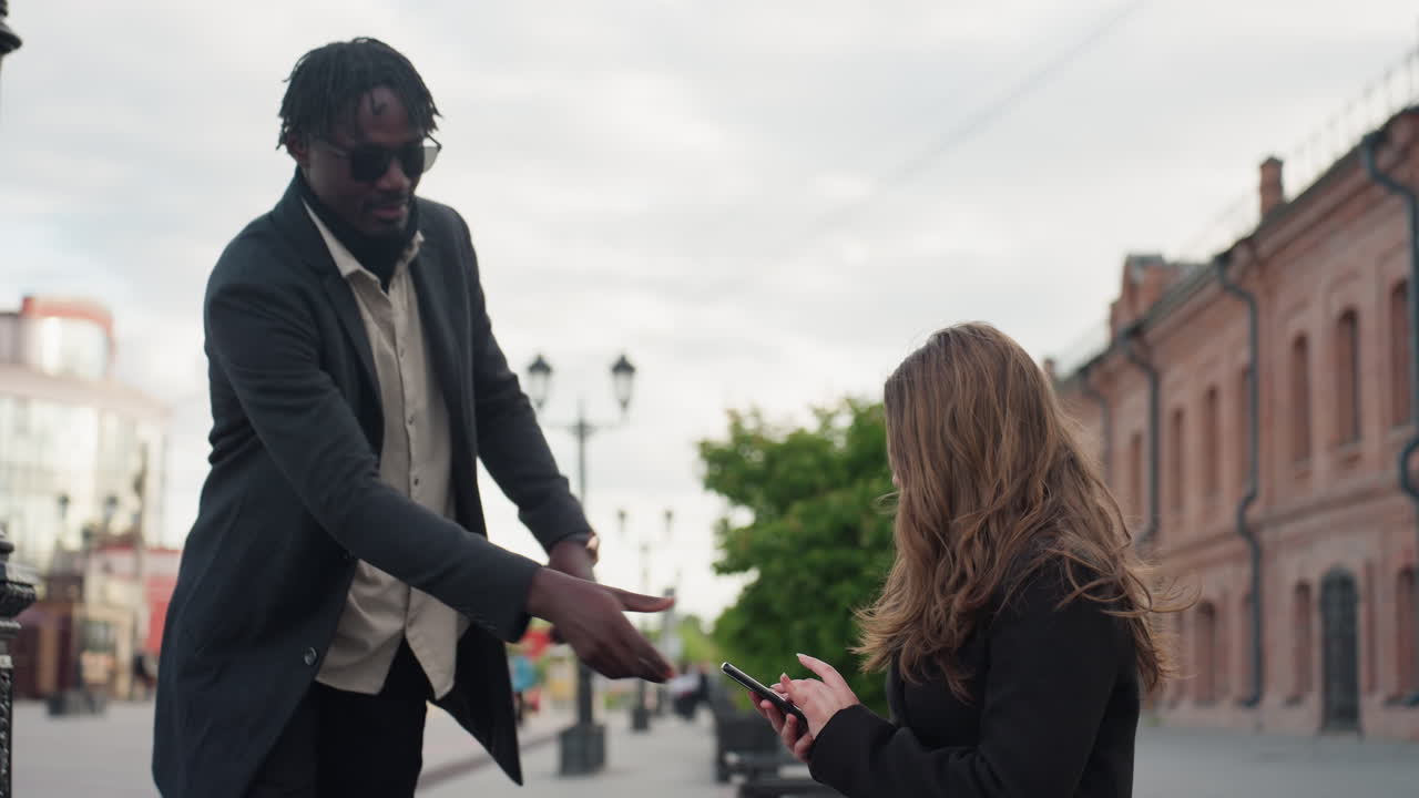 Female adult chases after partner along city street lined with vintage brick buildings and green trees under soft daylight, showing motion, emotion, and urban life within calm yet dramatic setting