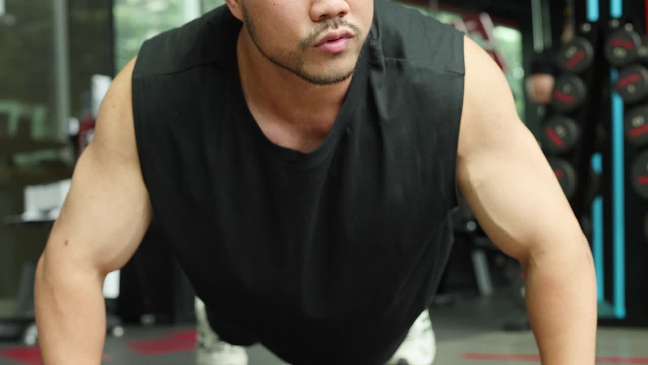 A determined man performs push-ups in a gym, showcasing strength and concentration under bright lighting
