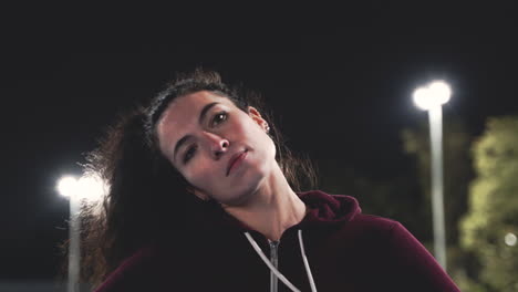 portrait of a sportive curly girl stretching neck before training in the park at night