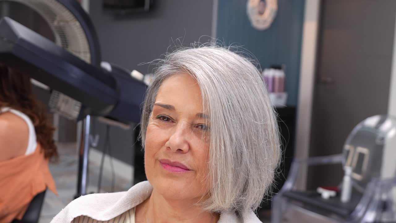 Hairdresser Blow Drying and Styling Senior Woman's Gray Hair in Salon