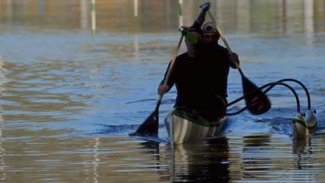 Two men paddling an outrigger canoe on a water course