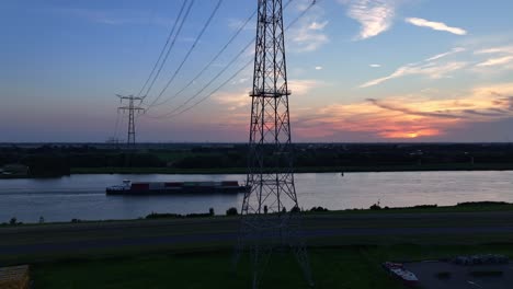 a barge moves along a calm river at sunset with power lines crossing overhead