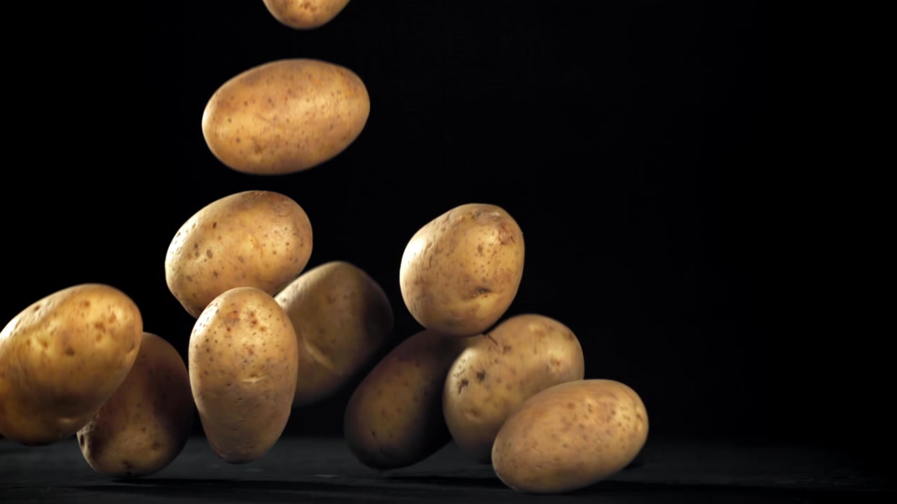 Patate fresche e crude che cadono al rallentatore su sfondo nero