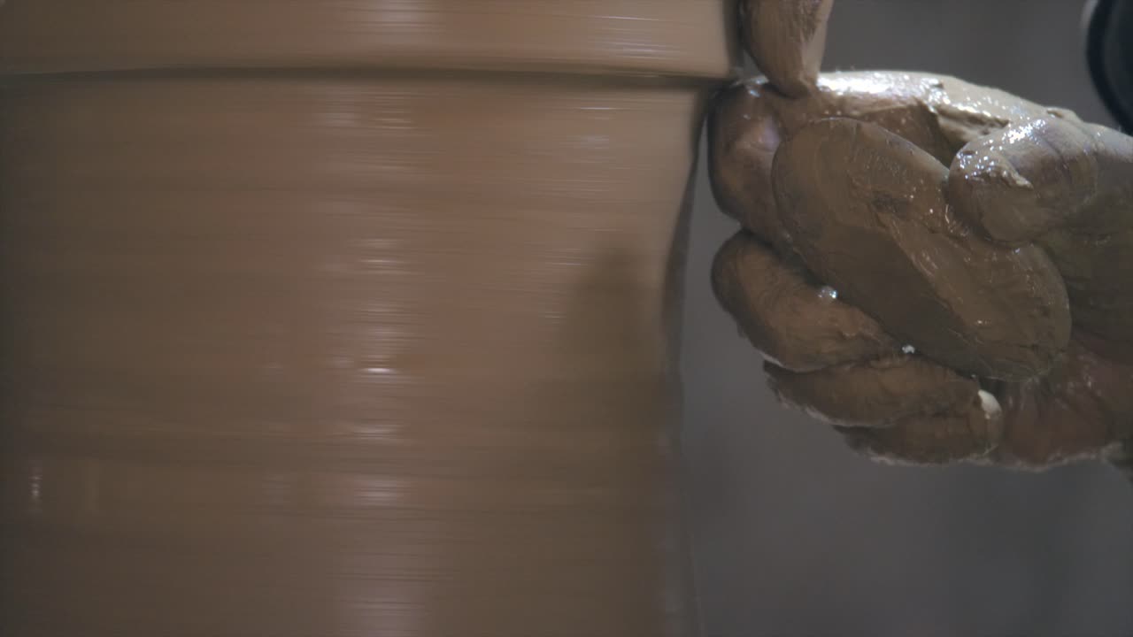 Primissimo piano di un vasaio che usa un raschietto per levigare e intagliare i bordi sottili di un vaso di argilla.
