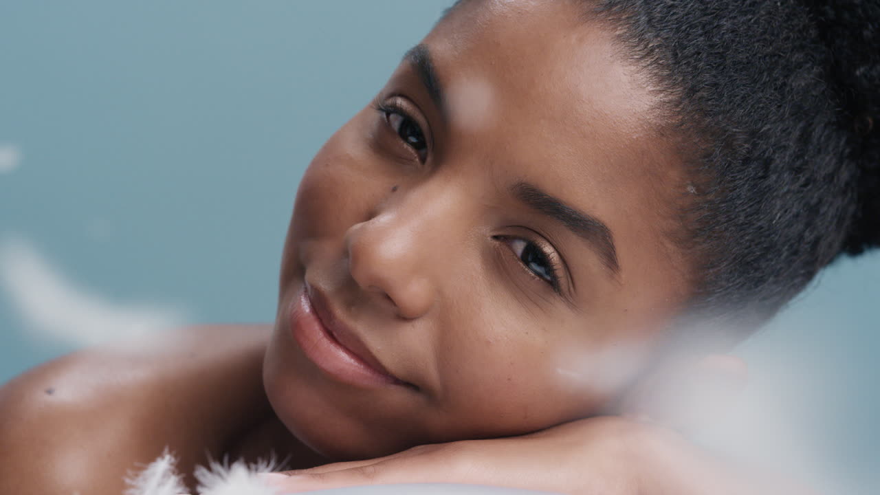 close up portrait beautiful young african american woman relaxing feathers falling on soft natural skin gently caressing healthy complexion in slow motion skincare concept