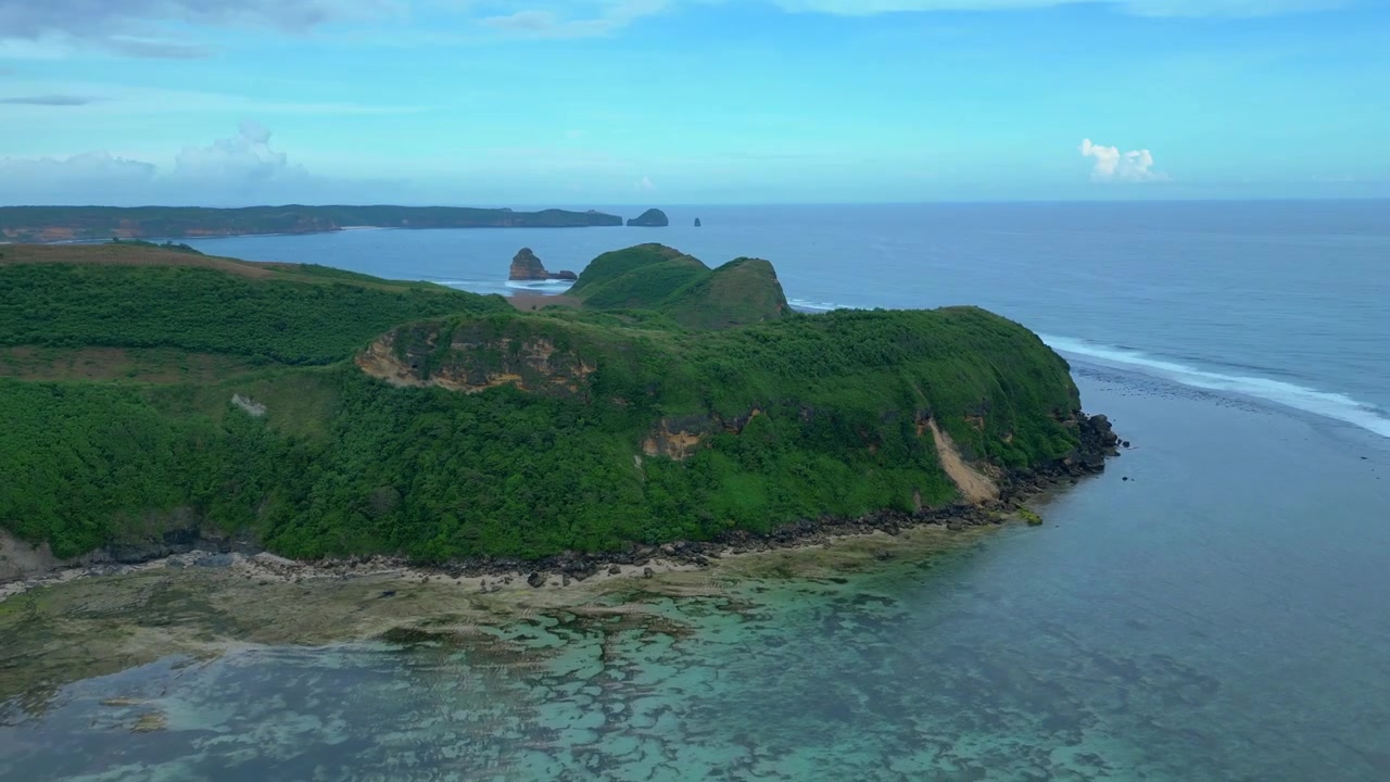 Vista della costa dell'isola di Lombok che mostra lussureggianti colline verdi, un sentiero tortuoso, onde oceaniche distanti e acqua limpida e poco profonda. Favolosa vista aerea, ampio panorama orbitale, panoramica con drone, speed ramp, hyper motion
