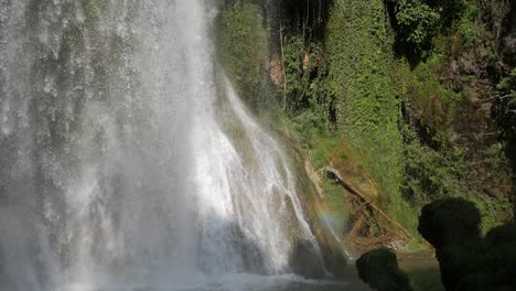 beautiful downpour cataract waterfall on plunge pool. water stream drop on rocks and pool surrounded by vegetation. sun rays create a rainbow colour spectrum halo on one side