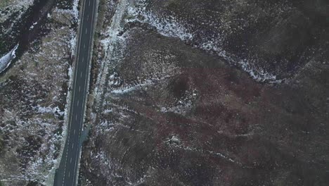 Single-white-vehicle-on-a-remote-road-in-Skye,-dusting-of-snow-on-the-landscape,-aerial-view