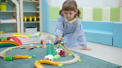 girl toddler plays with toy car, moving truck along road sitting on floor at playroom