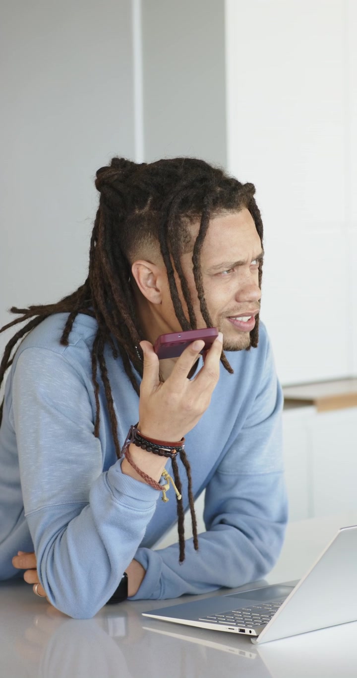 Vertical video: Reaching for purple phone man talking on speakerphone while scanning PC on counter
