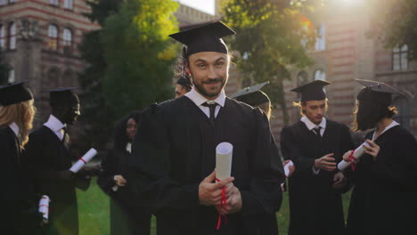 portrait of a young man graduate standing in traditional graduation clothes with diploma in hands and looking to the sky with hope