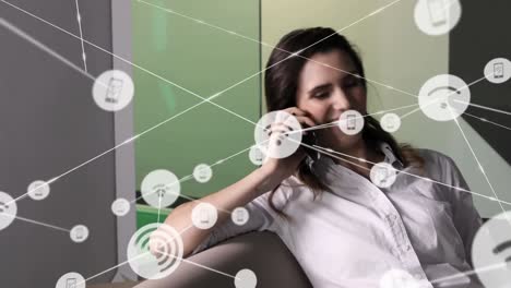 Animation-of-network-of-connections-with-icons-over-caucasian-businesswoman-talking-on-smartphone