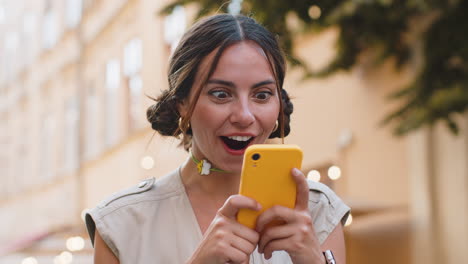 Excited-happy-winner-young-woman-use-smartphone-celebrating-win-good-message-news-in-city-street