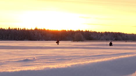 Tiro-Deslizante-De-Hombres-Pescando-En-Hielo,-Sobre-Hielo-Cubierto-De-Nieve,-Al-Atardecer,-En-Una-Soleada-Tarde-De-Invierno,-En-Ostrobotnia,-Finlandia