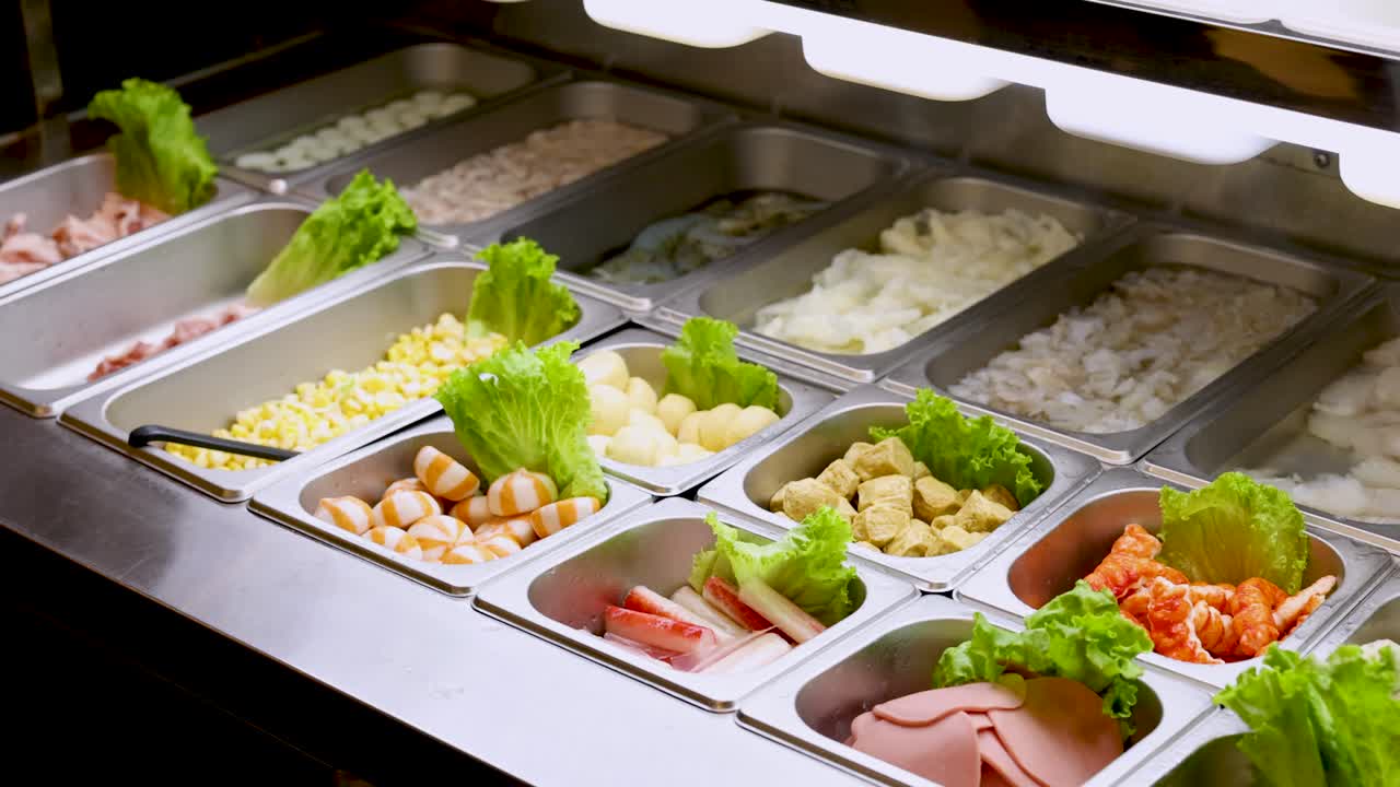 Camera pans across self-service buffet with assorted hotpot ingredients under bright, even lighting
