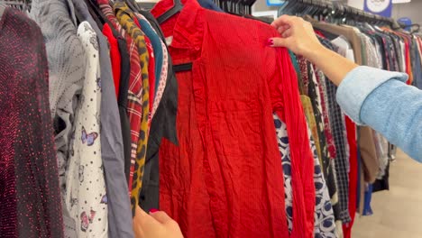 young woman selecting fuchsia sweater in dressing room, carefully examining sleeve length, checking appearance in mirror while making expressive gestures. concept of buying women clothes