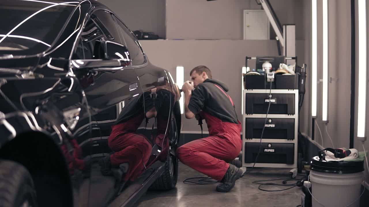 trabajador en traje rojo limpiando un coche caro negro.