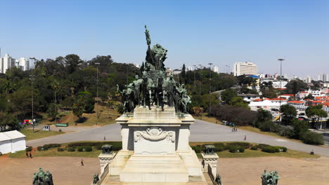 Cámara-Volando-Hacia-Abajo-Y-Lejos-Del-Monumento-A-La-Independencia-En-El-Parque-De-La-Independencia-Con-El-Museo-Ipiranga-En-El-Fondo-De-La-Escena