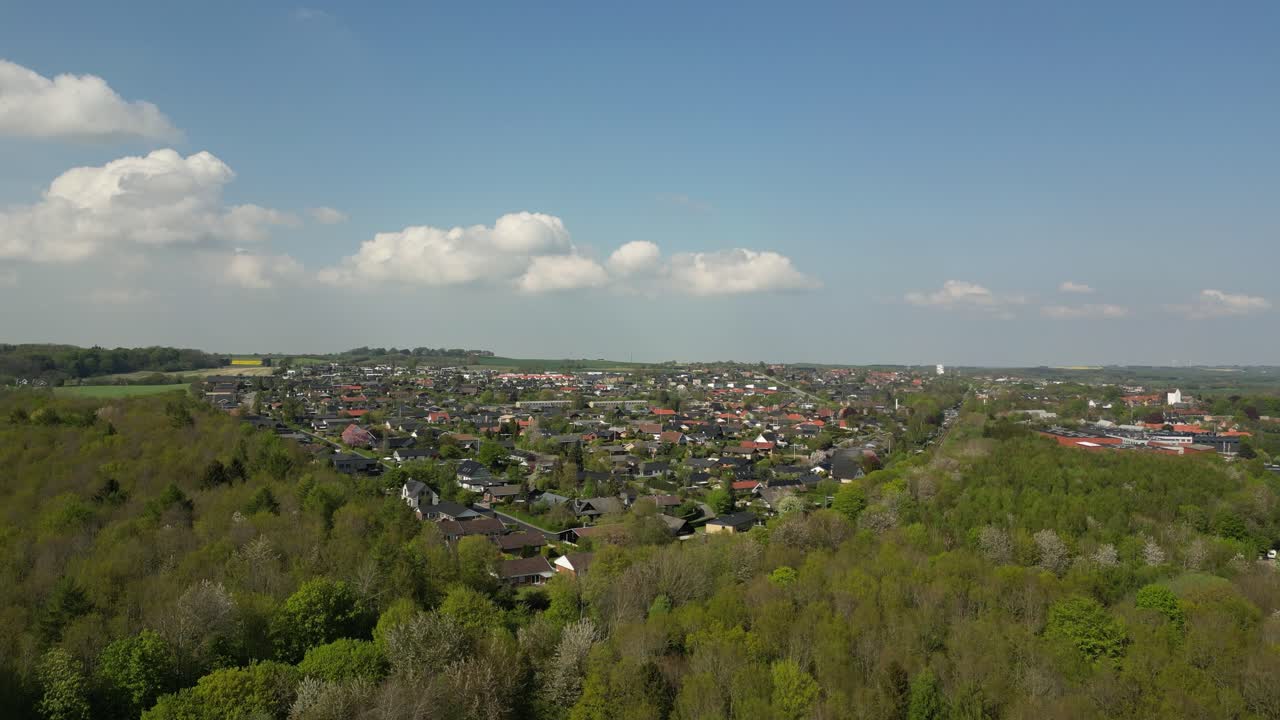 드론이 숲 위로 천천히 상승하는 숲의 드론으로 촬영된 영상, 그리고 배경에는 스코드스트루프 마을이 눈에 띄고 있습니다.