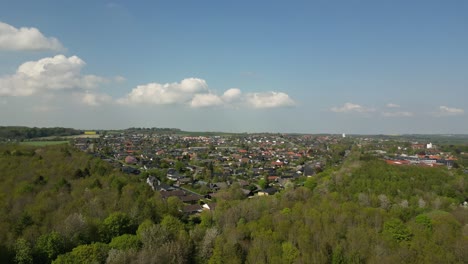 Imágenes-Tomadas-Con-Un-Dron-De-Un-Bosque,-Donde-El-Dron-Se-Eleva-Lentamente-Sobre-El-Bosque-Y,-Al-Fondo,-Se-Ve-La-Ciudad-De-Skødstrup.