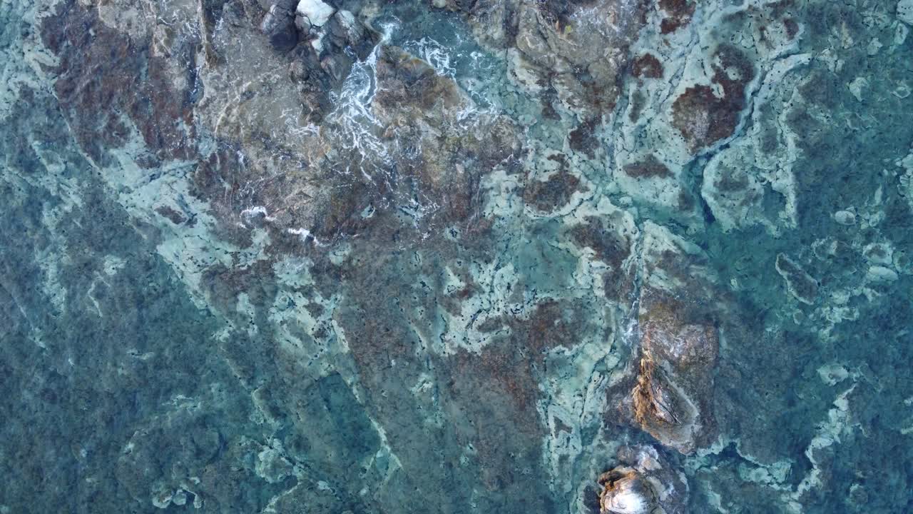 Amazing rock formations under the sea with waves crashing above | Steady aerial shot over clear turquoize sea | 4K
