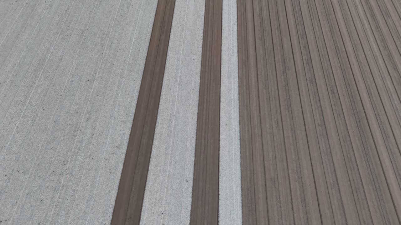 slow-motion drone shot reveals perfectly parallel strips of pale tilth and rich brown earth freshly leveled across a vast field forming an orderly grid poised for the next planting season